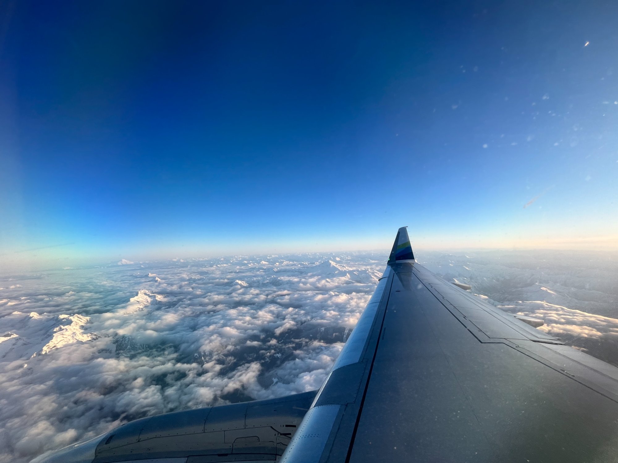 Alaska Airlines wing over snowy mountains and clouds