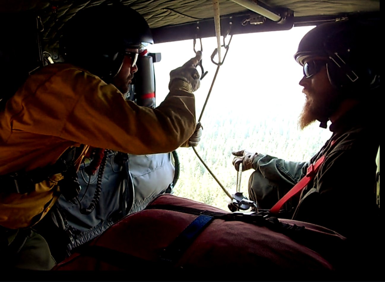 Ken in helicopter with rappel gear over forest